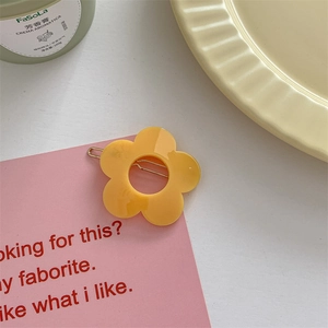 Detailed macro of a yellow acrylic flower hair clip with a gold metal barrette base