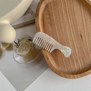 Macro shot of an iridescent pearlescent wide-tooth hair comb on a minimalist wooden tray