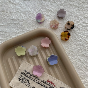 Mini pinces à cheveux en acétate aux couleurs pastel sur un plateau beige minimaliste