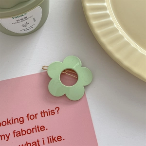 Detailed close-up of a mint green flower hair clip with a metal base on a decorative setup