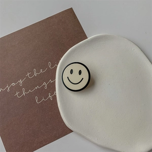 Support téléphone beige avec motif smiley sur un plateau blanc au style minimaliste