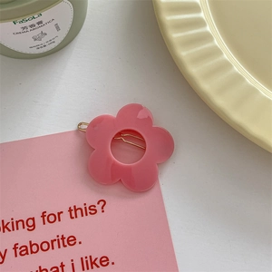 Detailed view of a cute pink flower hair clip with a golden metal pin on a pastel tray
