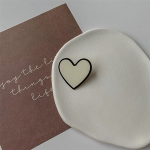 Détail macro d'une pince en forme de cœur avec émail crème et bordure noire élégante