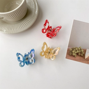 Three acetate butterfly hair claws in red and marble patterns on a white table