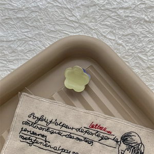 Détail de mini pince à cheveux fleur en acétate jaune et bleu sur un plateau beige