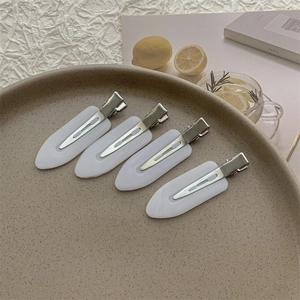 Close-up of four white leaf-shaped seamless hair clips displayed on a decorative tray