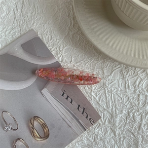 Detailed view of an oval resin hair clip with pink sequins on a white textured backdrop