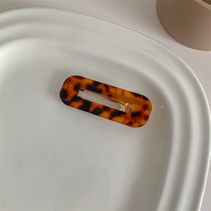 Detailed close-up of amber acetate hair clip with golden metal fastener on ceramic