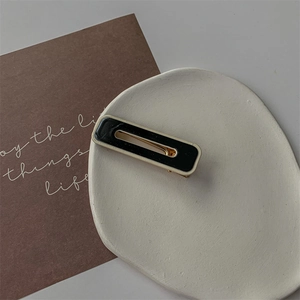 Détail d'une pince à cheveux rectangulaire noir et or sur un plateau en céramique