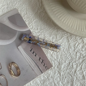 Detail of a resin hair clip with purple shell flakes next to a golden twisted ring