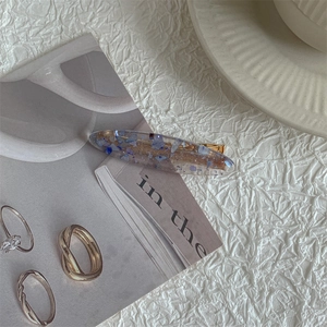 Detailed view of an oval blue floral resin hair clip on white textured fabric