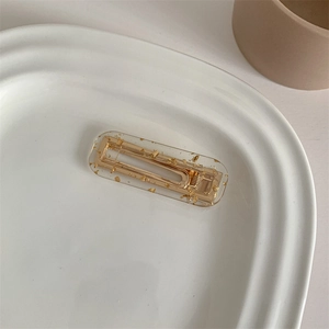 Detail of a rectangular resin hair clip with gold foil flakes on a ceramic plate
