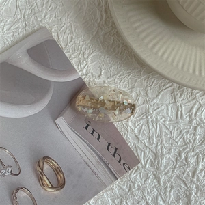 Macro detail of oval transparent resin hair clip with iridescent shell flakes and metal base