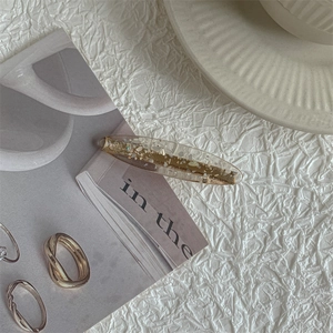 Close-up of an oval hair clip with gold foil and shell fragments on white crinkled paper