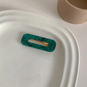 Detail of dark green marble pattern hair clip with gold metal on white tray