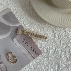 Detail of a rectangular resin hair clip with colorful iridescent shell fragments inside