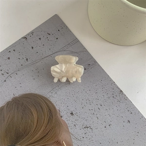 Detail of elegant cream marble acetate hair claw clip on minimalist textured background