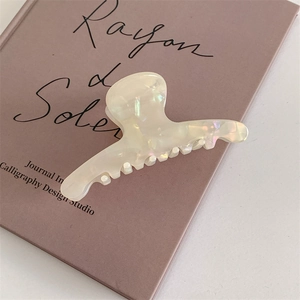 Macro shot of elegant cream acetate hair claw clip with mother of pearl finish on art book
