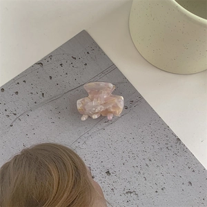 Detail view of a small pink and beige marble pattern cellulose acetate hair claw clip