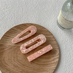 Lot de 3 barrettes en acétate rose à texture marbrée sur un plateau en bois