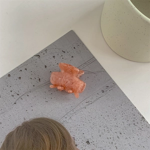 Detail of a peach marble texture acetate hair claw clip on a textured grey background