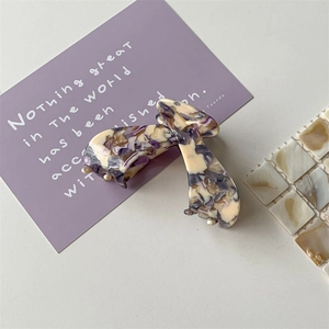 Detail of a marbled acetate hair claw clip with purple and cream textures on white tiles