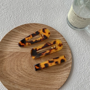 Détail de trois barrettes en acétate à motif écaille de tortue sur un plateau en bois