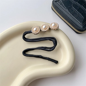 Detail showing a black hair bun maker with elegant faux pearls on a cream display tray