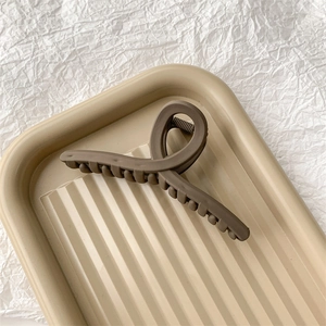 Détail d'une grande pince à cheveux marron mat sur un plateau beige élégant