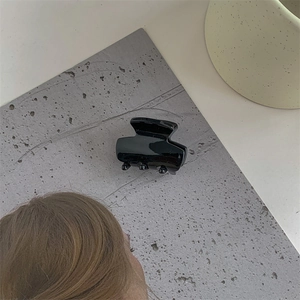 Detail of a minimalist black acetate hair claw clip on a stylish textured grey surface