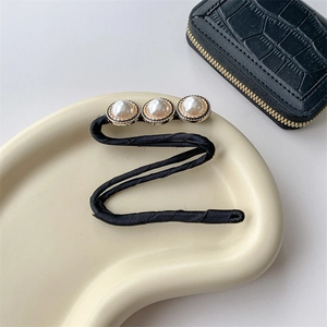 Detailed macro view of an elegant black fabric bun maker with three white faux pearls