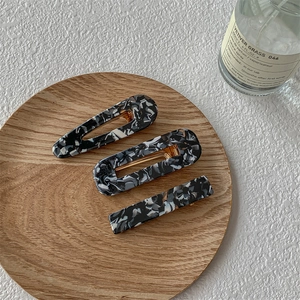 Lot de trois barrettes à cheveux à motif marbré présentées sur un plateau en bois