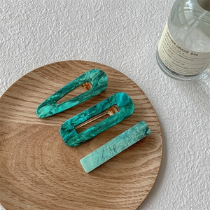 Détail de trois barrettes en acétate vert foncé à motif marbré sur un plateau bois