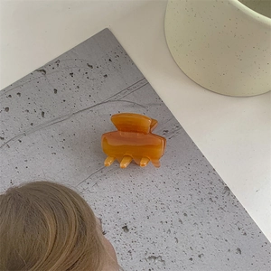 Detail view of a translucent amber acetate hair claw clip on a gray textured surface