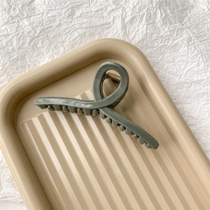 Vue détaillée de la grande pince à cheveux mate vert olive sur un plateau texturé