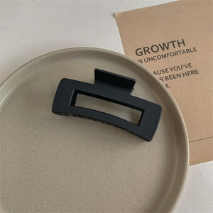 Detailed close-up of a large matte black rectangular shark hair claw clip on a beige tray