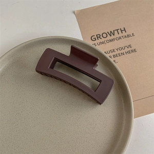 Detail showing matte coffee brown rectangle hair claw clip on a ceramic tray with soft shadows