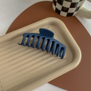 Navy blue matte shark hair claw clip displayed on a minimalist decorative beige plate