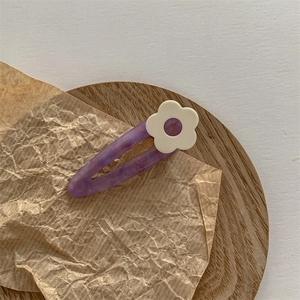 Détail d'une pince à cheveux fleur en acétate marbré violet sur plateau en bois