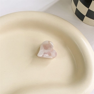 Detailed view of heart-shaped acetate hair claw with pink marble texture on ceramic plate