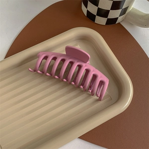 Detail of a large matte pink shark hair claw clip on an elegant beige lifestyle background