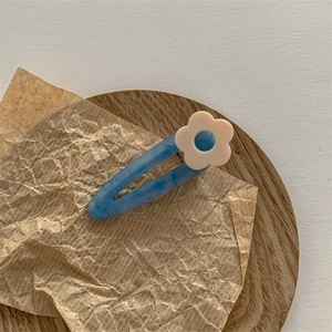 Détail d'une pince à cheveux marbrée bleue avec une petite fleur beige sur bois