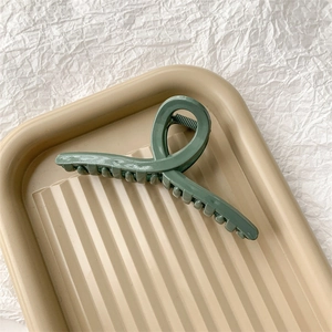 Détail de la grande pince à cheveux vert Morandi avec design croisé et finition brillante