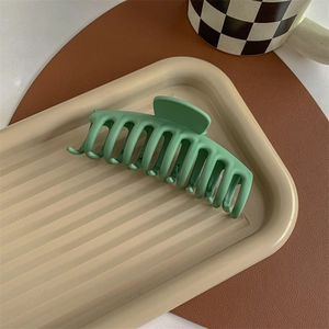 Detail of large matte green shark hair claw clip on aesthetic beige tray setting