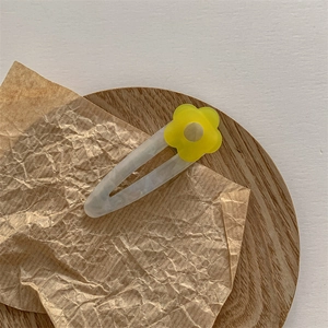 Détail d'une pince à cheveux fleur jaune effet marbre sur un plateau en bois