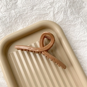 Détail d'une pince à cheveux marron latte au design croisé élégant sur un plateau