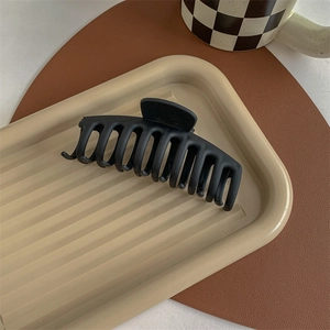 Detail of a large matte black hair claw clip resting on a wavy decorative tray