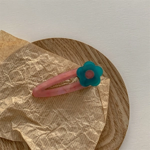 Détail de la pince à cheveux en acétate rose marbré avec fleur bleue sur fond en bois