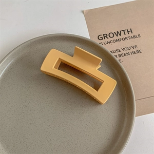 Detailed close-up of a matte mustard yellow rectangular claw clip on a grey tray