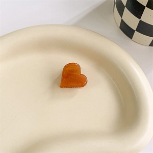 Close-up of heart-shaped amber acetate hair claw clip on a minimalist ceramic tray